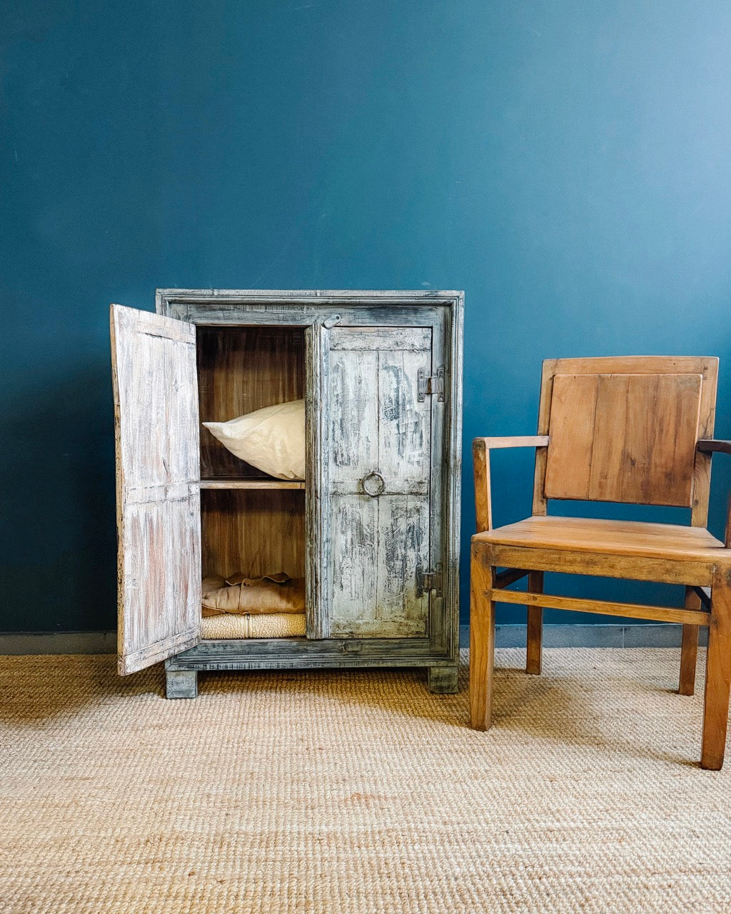 Restored reclaimed wood cabinet with original patina and iron ring pull, beside a vintage teak armchair