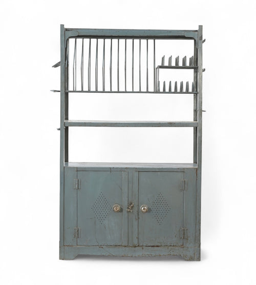 Vintage iron kitchen rack with blue-grey paint patina, featuring plate slots, cup hooks, and a lower cabinet.