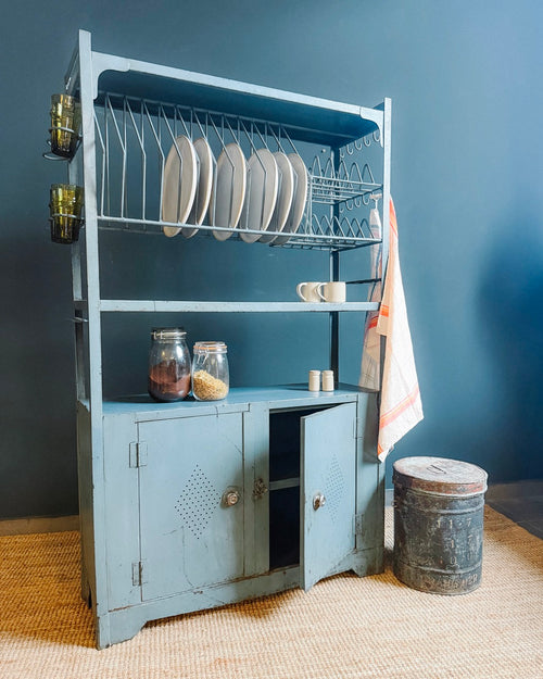 Vintage-style blue kitchen cabinet with shelves against a dark blue wall.