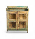 A vintage reclaimed wood glass cabinet with aged paint in soft yellows, weathered green, and turquoise, featuring glass panelled doors and a built-in shelf.