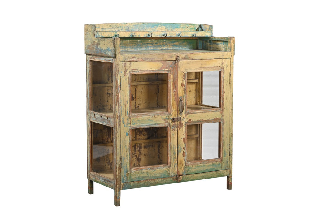 A vintage reclaimed wood glass cabinet with aged paint in soft yellows, weathered green, and turquoise, featuring glass panelled doors and a built-in shelf.