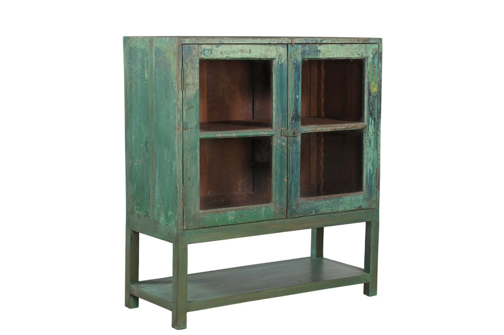A vintage teak wood glass display cabinet with green paint on the exterior and brown interior, featuring two glass panelled doors with a single shelf.