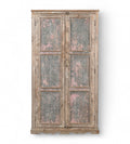A vintage teak wood wardrobe with iron panels, featuring a carved base and an aged patina finish in soft pink and faded grey.
