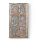 A vintage teak wood wardrobe with iron panels, featuring a carved base and an aged patina finish in soft pink and faded grey.