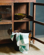 A wooden teak bucket with a checkered towel draped over it on the floor.