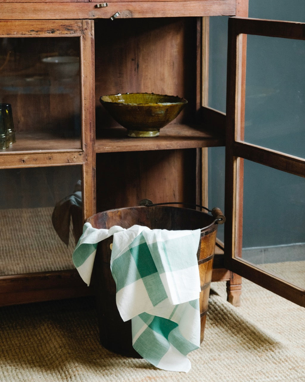 A wooden teak bucket with a checkered towel draped over it on the floor.