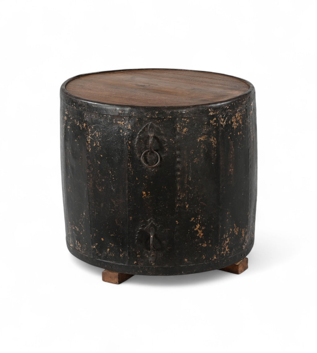 A cylindrical vintage side table made of iron with a teak wood top, featuring ring handles and a worn black finish.