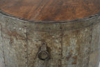 A cylindrical vintage side table made of aged iron with a teak wood top, featuring ring handles and a weathered finish.