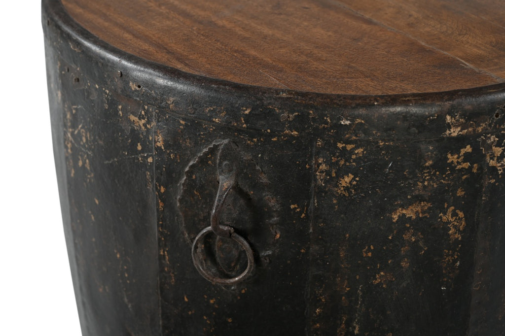 A cylindrical vintage side table made of iron with a teak wood top, featuring ring handles and a worn black finish.
