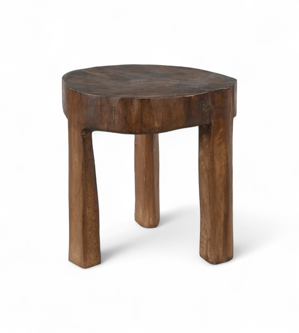 A vintage Indian teak wood stool with an irregular shape and a dark patina, indicating age and use.