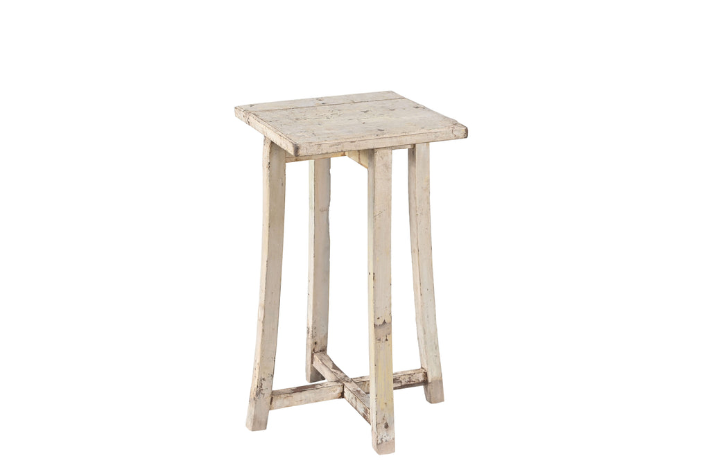 A vintage teak wood side table with subtly curved legs and a cross stretcher base, with a creamy white finish.