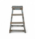 A vintage teak wood bar stool with a faded soft blue patina and iron brackets.