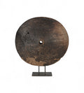 A large circular teak wood wheel with visible cracks and grooves, mounted on a metal iron stand.