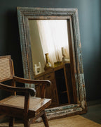 Large ornate mirror with a wooden frame in a room with a chair and furniture.