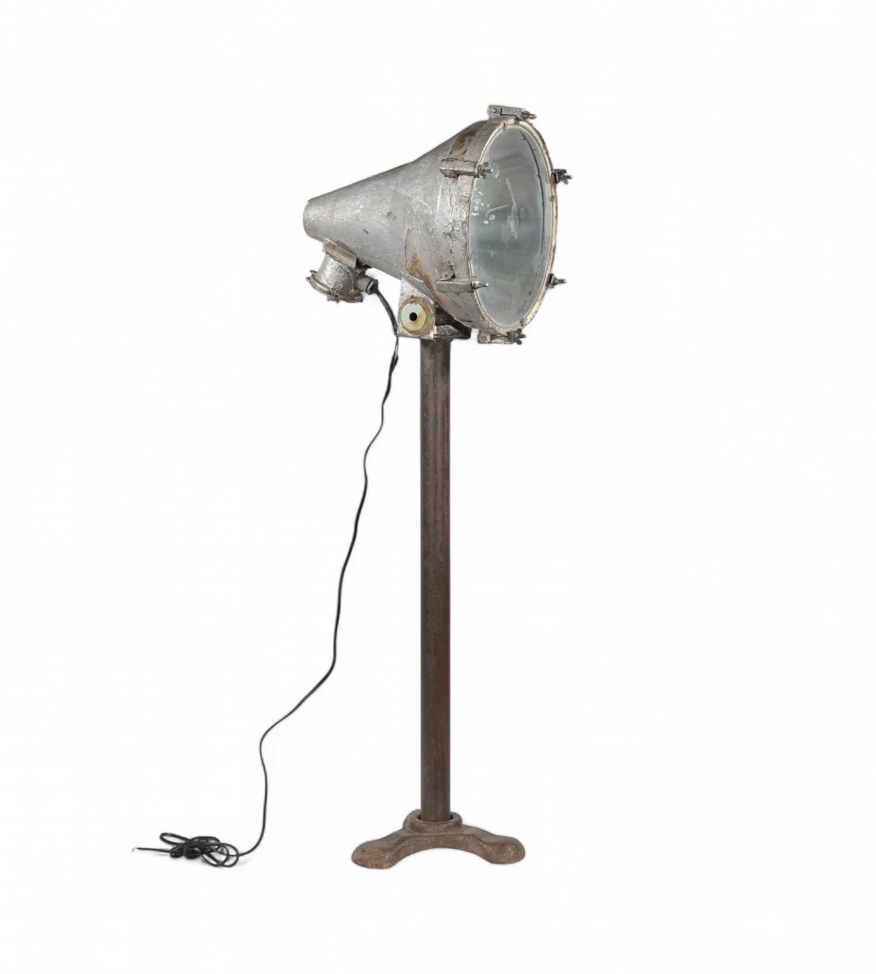 A vintage industrial style floor lamp with a cast iron base and a pivoting spotlight head, featuring a heavy duty lens and visible wiring.