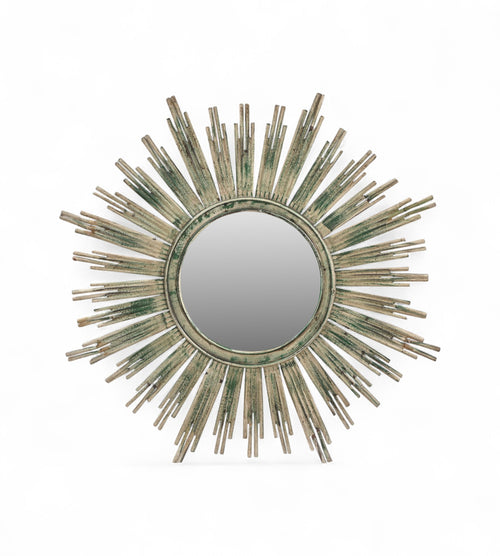 A round iron mirror frame with a sunburst design, featuring rays in green, yellow, and brown hues.