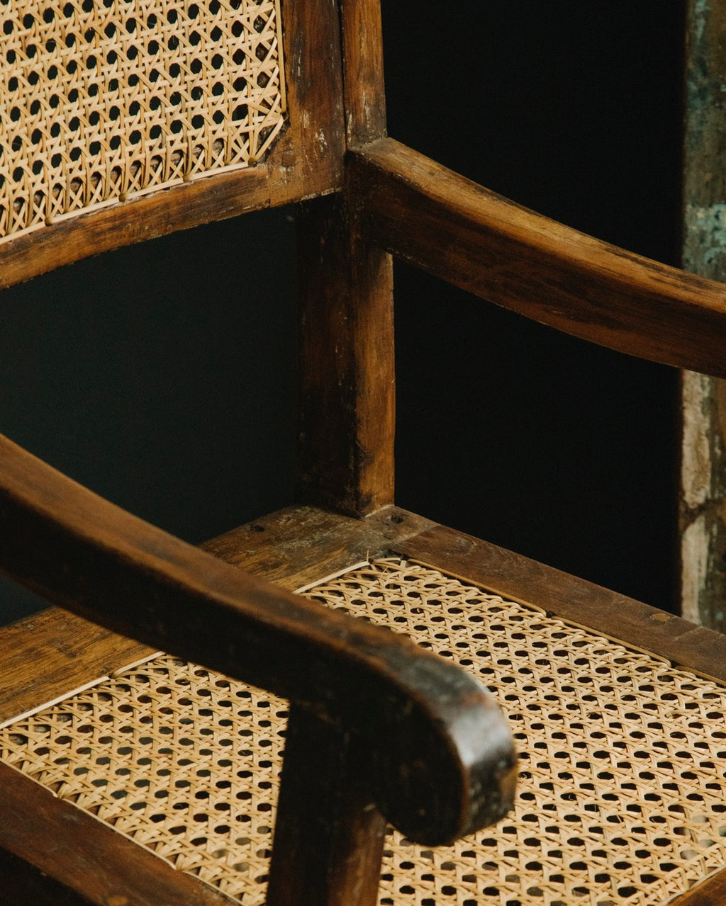 Close-up of a wooden chair with wicker seat and backrest against a dark background